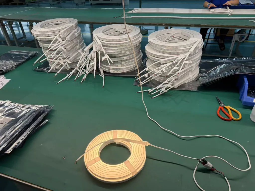 Silicone neon flex light rolls stacked neatly on a green manufacturing table with connectors, scissors, and a glowing sample light.