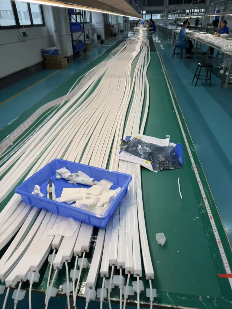 A production line with silicone neon flex strips being assembled, featuring connected strips, tools in a blue tray, and workers in the background.