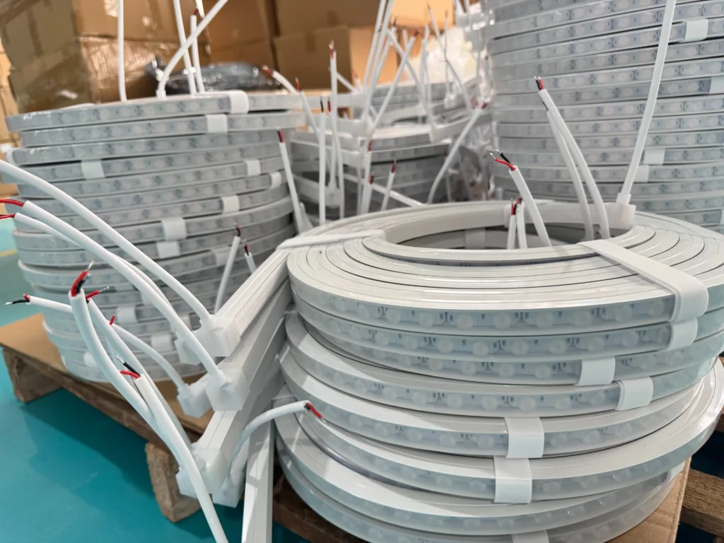 Multiple coils of silicone neon flex lights stacked in a factory setting, with visible connecting wires and packaging materials.