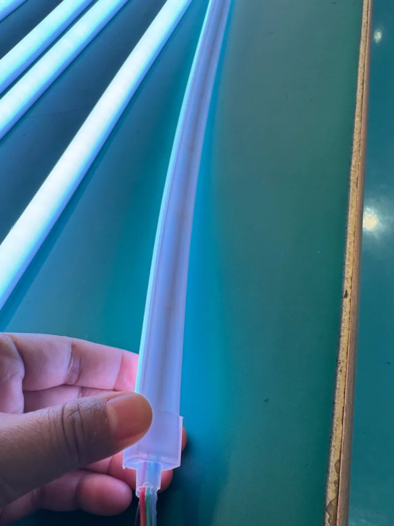 Close-up of flexible silicone LED light held by a hand on a teal surface, showcasing durability and light emission.