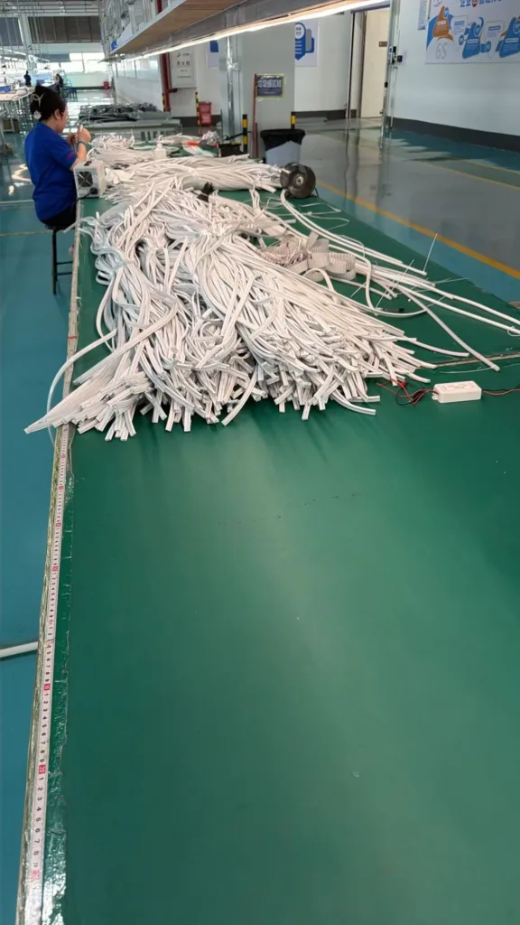 Worker assembling silicone neon flex strips on a production table in a factory setting, surrounded by organized materials.