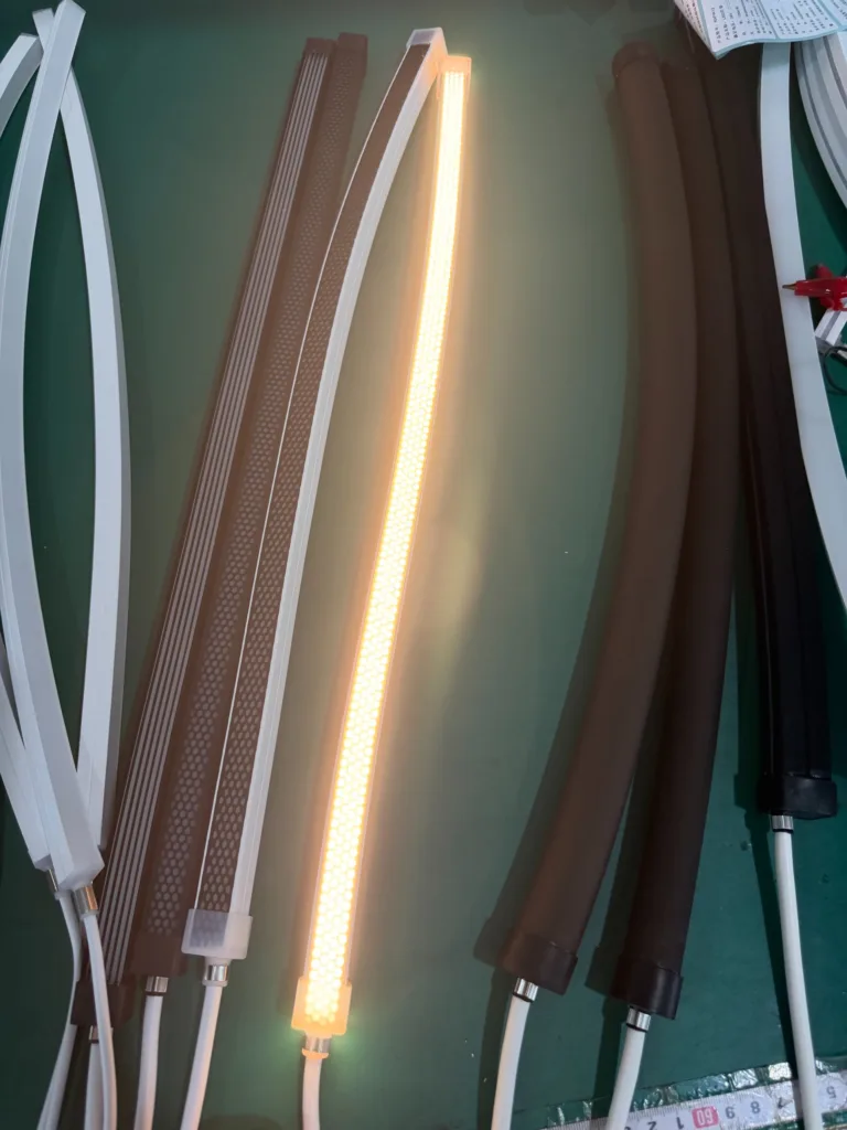 Various silicone neon flex lighting samples including illuminated warm white strip surrounded by black and white casings on a green surface.