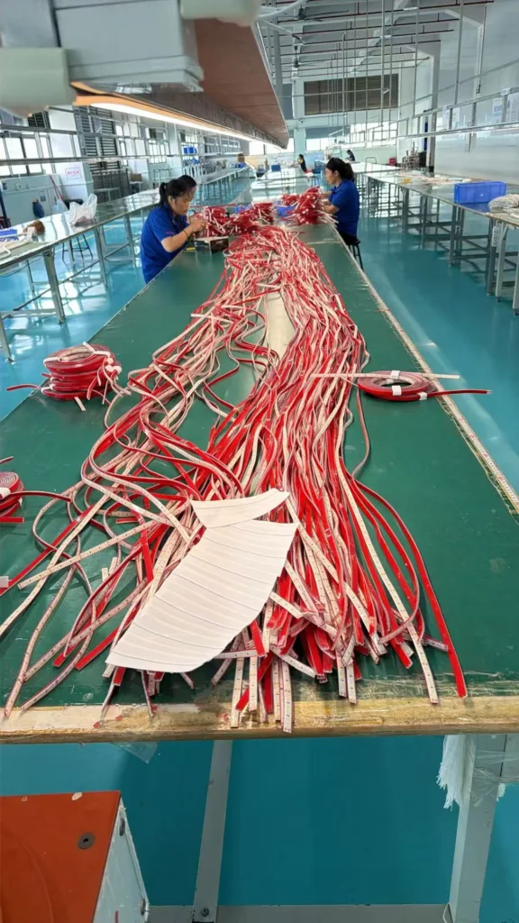 Manufacturing process with workers assembling red silicone neon flex lighting on large tables in a clean factory environment.