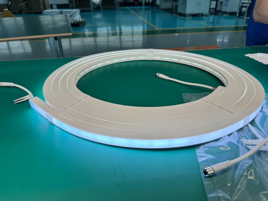 Coiled silicone neon flex light with connectors displayed on a green workspace in a manufacturing facility.