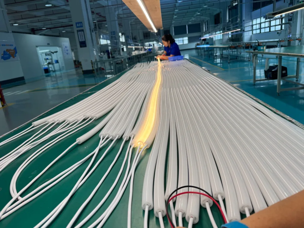Rows of white silicone neon flex lights being assembled in a spacious factory with modern equipment and overhead lighting.