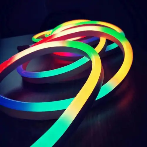 Coiled flexible RGB silicone neon strip light glowing in vibrant multicolor on a dark surface.