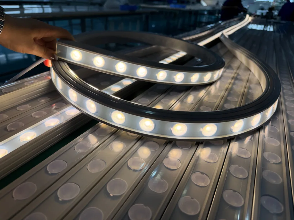 Close view of a hand holding flexible silicone LED strip lighting on a metal surface during production, with glowing LED diodes.