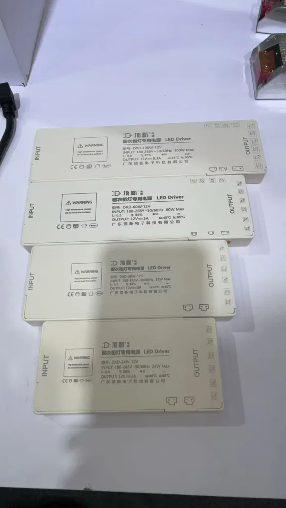 A selection of LED drivers of different capacities and specifications displayed on a table, each marked with input and output details.