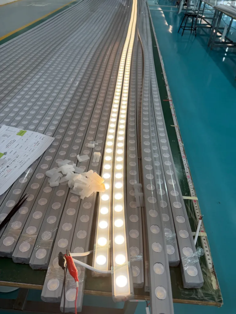 LED light fixtures on a production line, with one fixture illuminated emitting warm light, surrounded by silicone components.