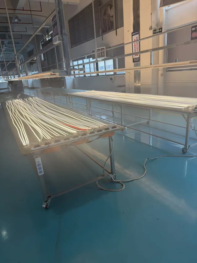 Production line with glowing LED silicone neon lights on metal tables in a well-lit manufacturing facility.