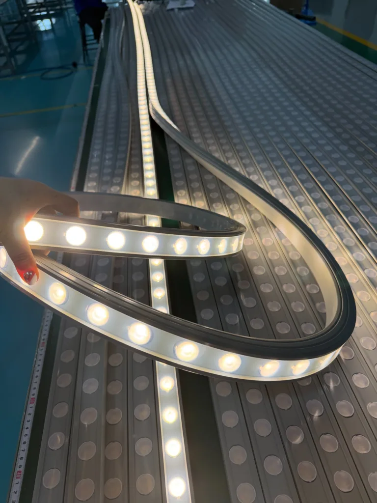 Close-up of LED silicone neon flex strips glowing warmly on production equipment, with a hand holding one strip.