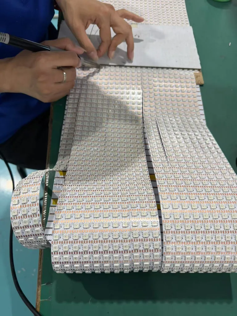 Hands inspecting and working on rolls of LED tape on a green workbench, ensuring quality control during production.