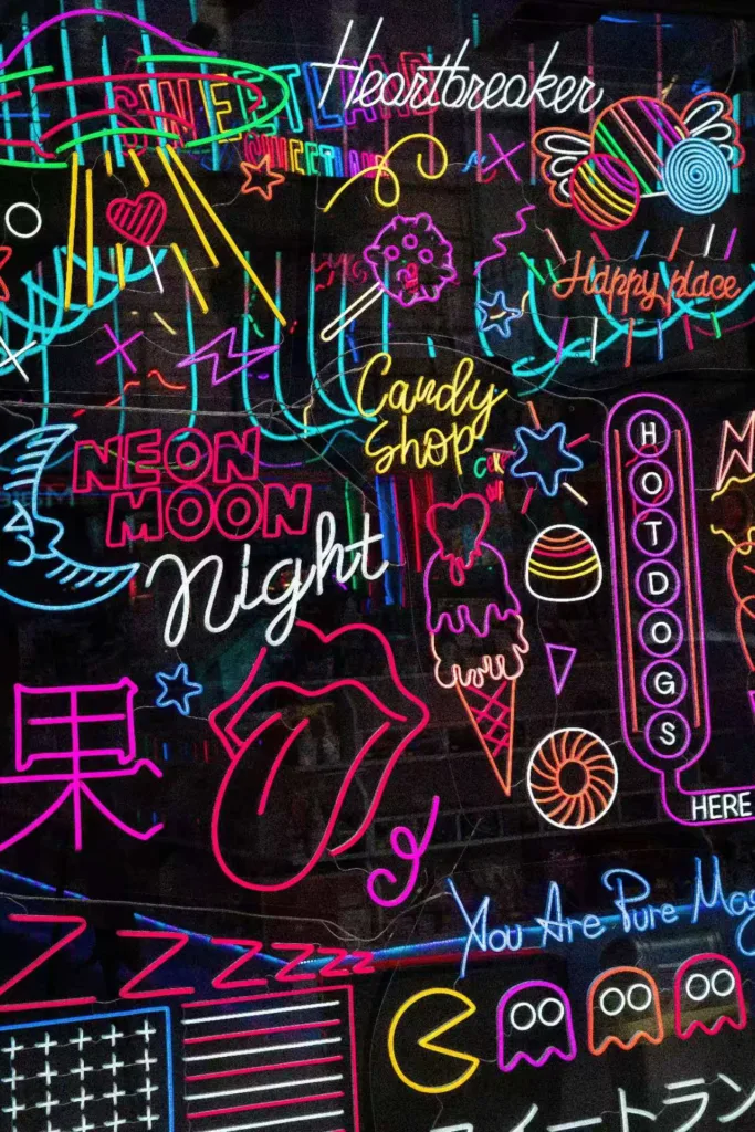 A vibrant collection of neon signs featuring abstract designs, including text like 'Candy Shop,' 'Neon Moon,' and playful graphics like a UFO, rolling lips, and Pac-Man ghosts.