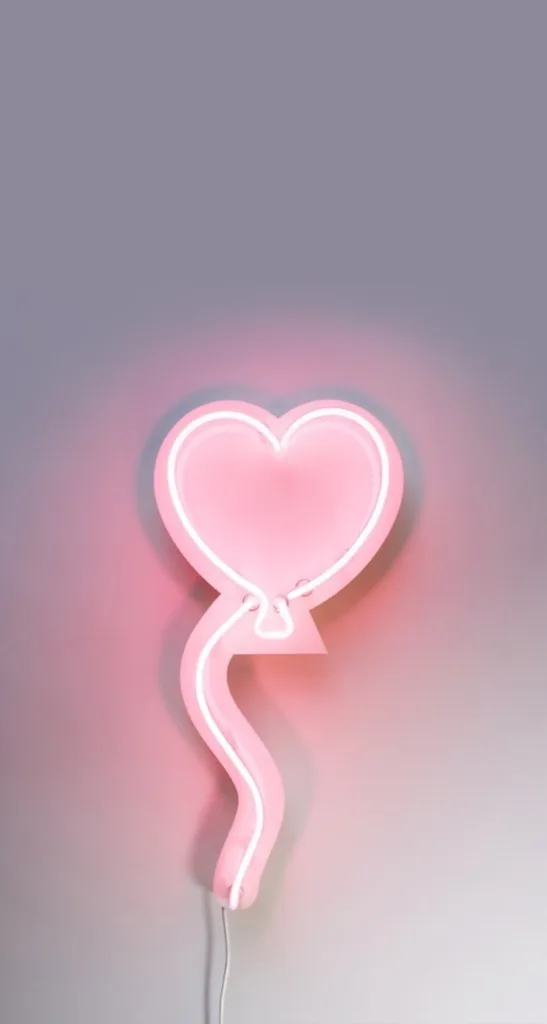 Pink heart-shaped neon light decoration with glowing soft pink hue and curved design mounted on a wall.