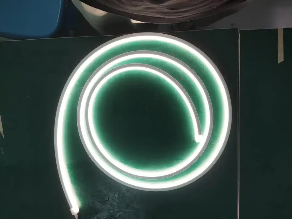 Coiled silicone neon flex lighting emitting white illumination on a dark, glossy surface.