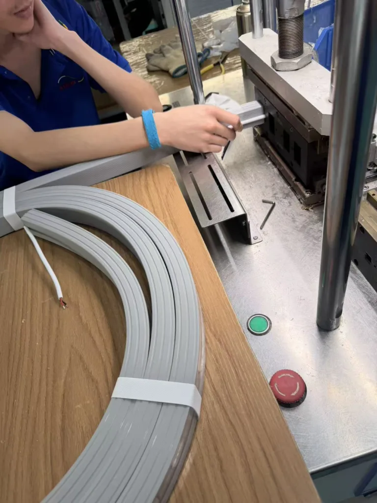 Worker assembling silicone neon flex lighting material using a machine on a wooden and metal workbench in a factory.