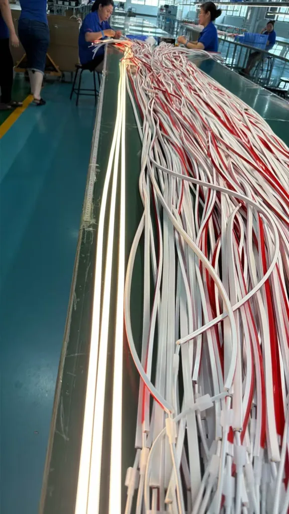 Workers inspecting silicone neon flex strips, with illuminated samples and neatly arranged production materials on a factory assembly line.