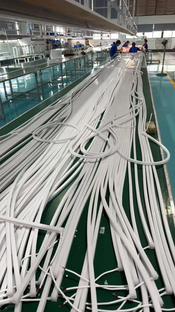 Spools of silicone neon flex on a production line with workers assembling lighting components in a factory.
