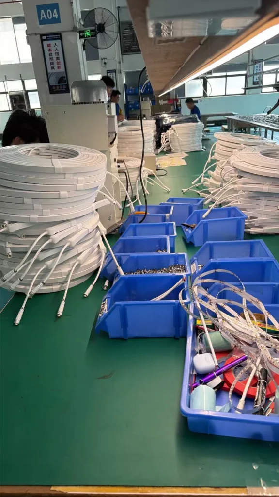 Silicone neon light components and assembled products on a green workbench in a manufacturing workshop with organized blue trays and coiled cabling.