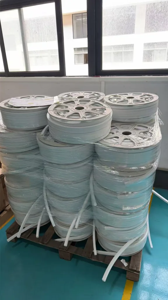 Multiple rolls of silicone neon flex lighting material stacked on a wooden pallet, wrapped in plastic film, inside a warehouse with large windows.