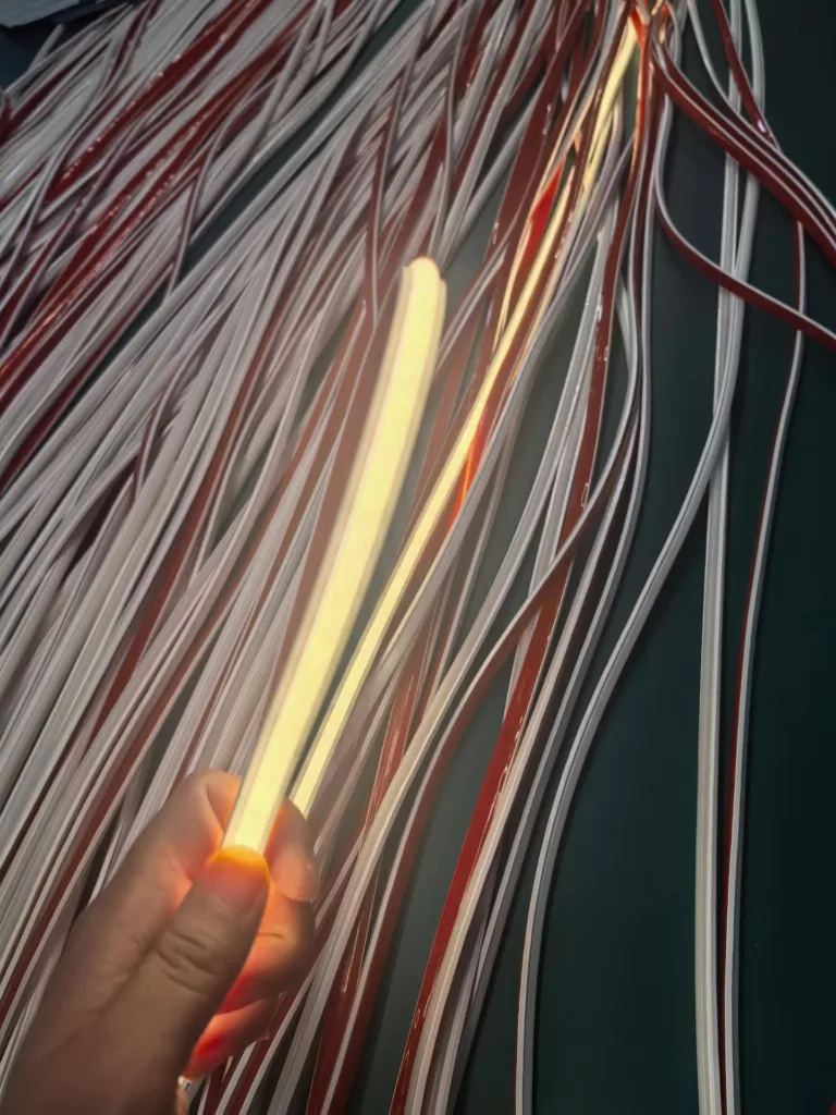 Hand holding a glowing silicone LED neon flex light surrounded by coiled silicone strips in red and white.
